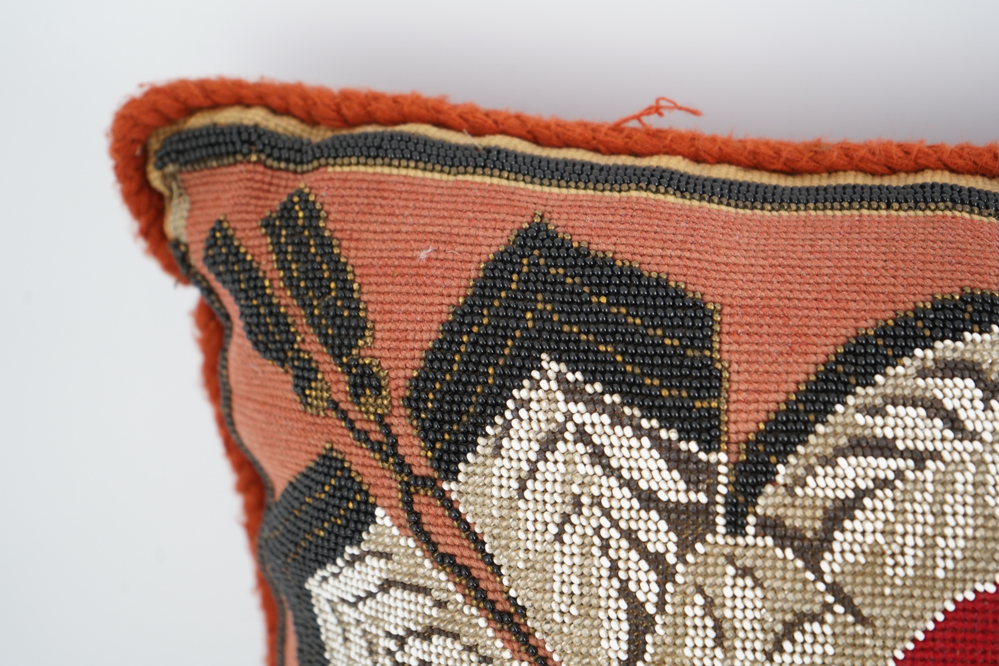 A 19th century Berlin bead worked cushion, the beadwork embroidered as a central rose, surrounded by an ornate tasseled swag, on a red wool worked background, 43cm x 45cm. Condition - some beadwork missing due to age and